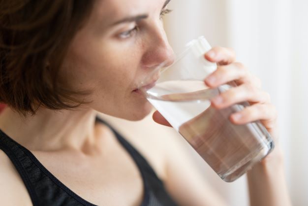 Žena drží skleničku s vodou v ústech a pije.